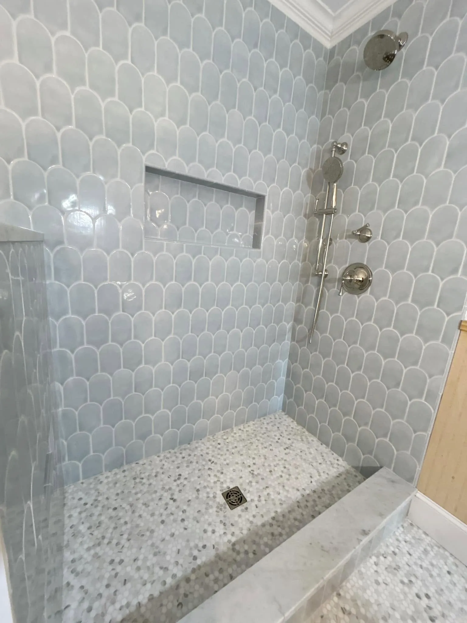 Blue scallop tile walk-in shower with a built-in niche, rain showerhead, and handheld fixture