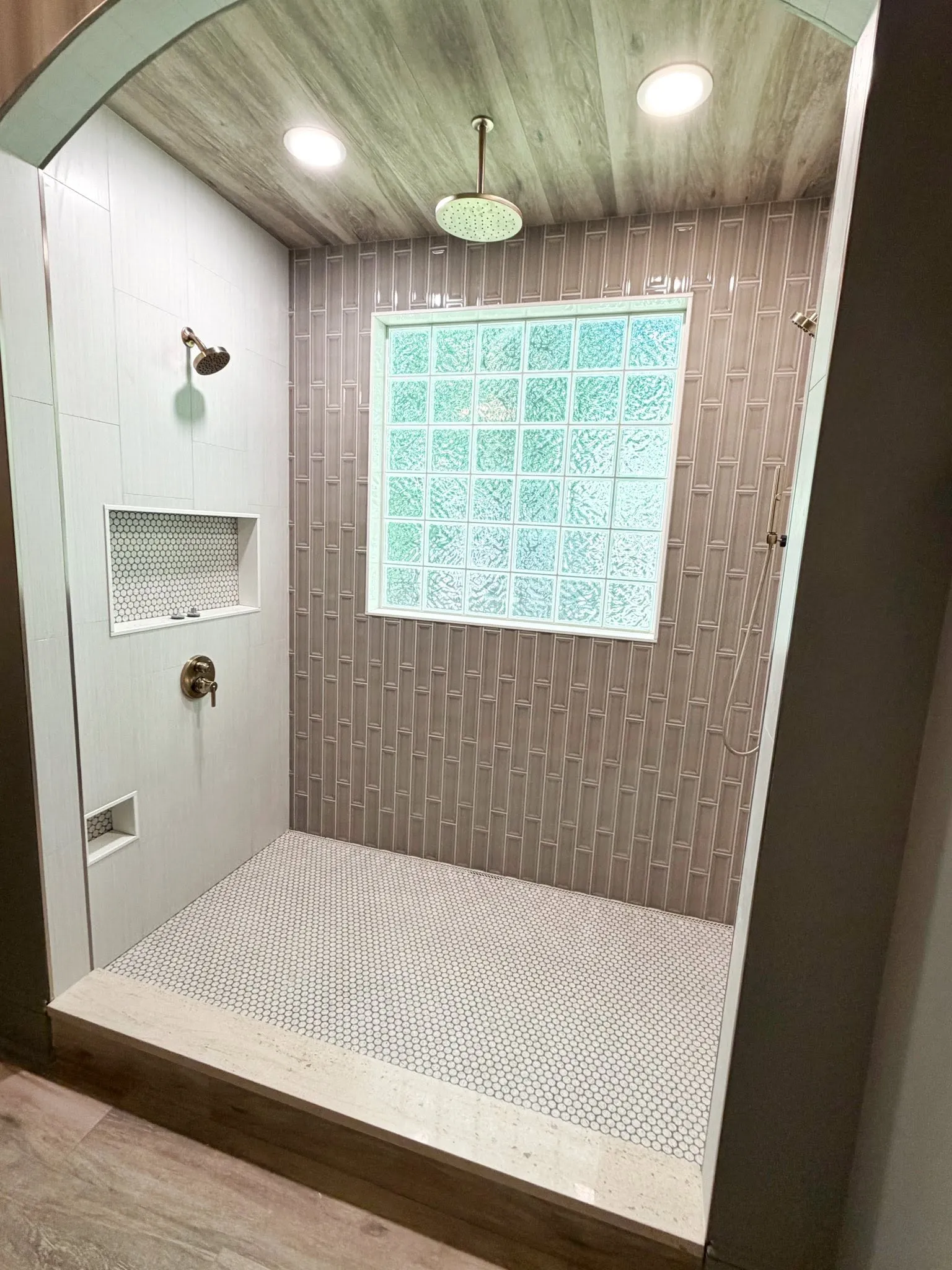 Large Cincinnati walk-in shower with a glass-block window, mosaic tile floor, and multiple showerheads