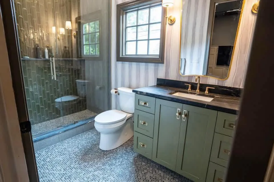 Completed bathroom remodel with a green vanity, glass-enclosed shower, and penny tile floor