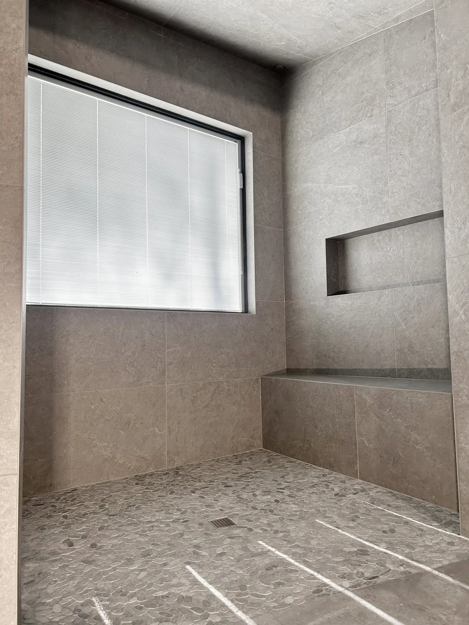 Large-format gray tile shower with a built-in bench, recessed niche, and pebble floor