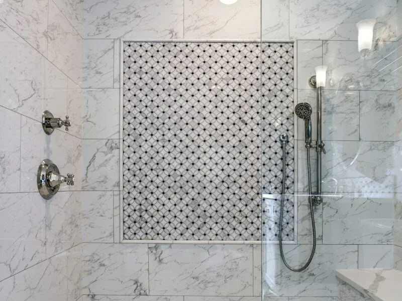 Marble tile shower with mosaic accent panel and glass door