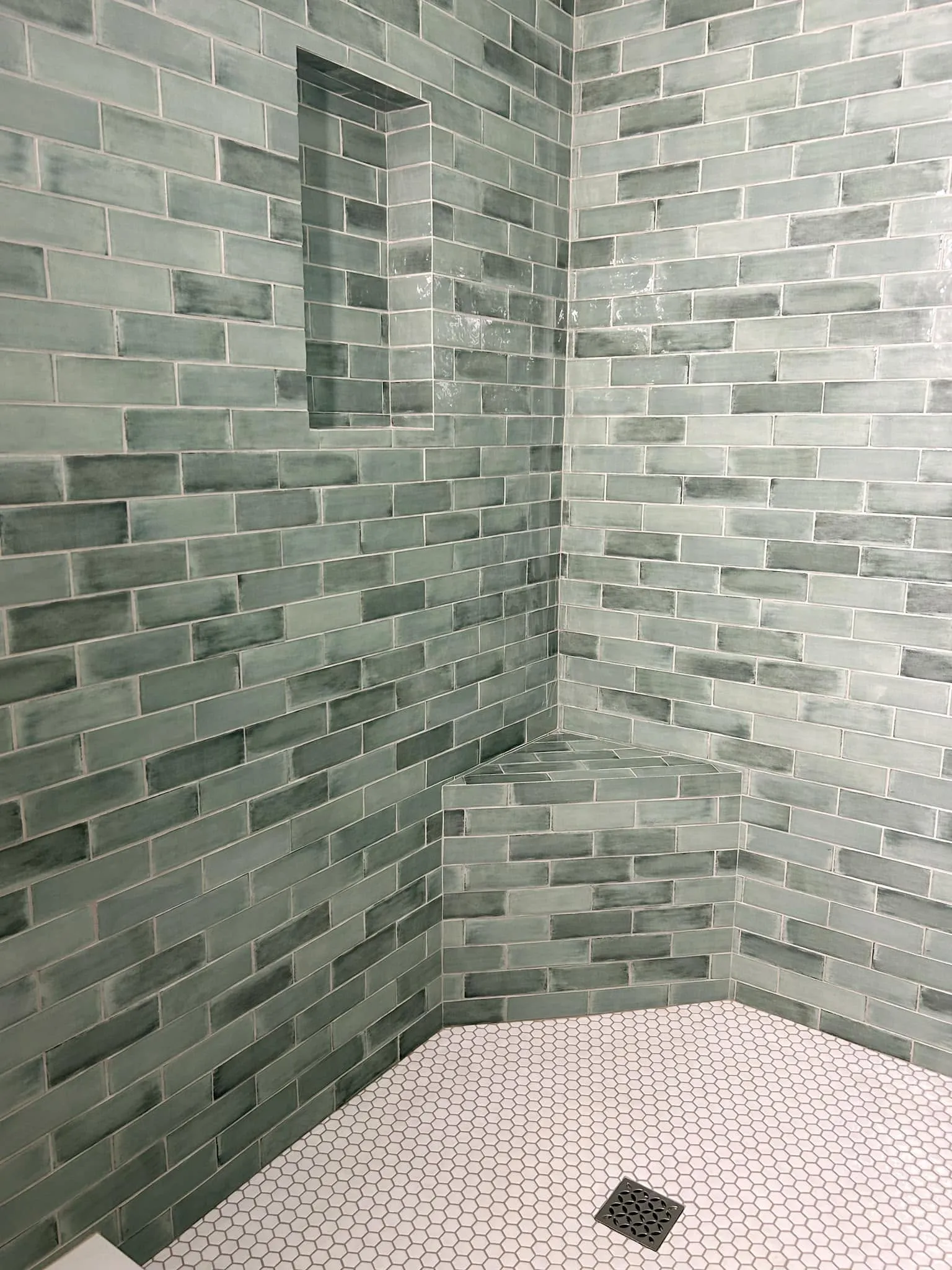 Sage green subway tile shower installation with a recessed niche and corner bench