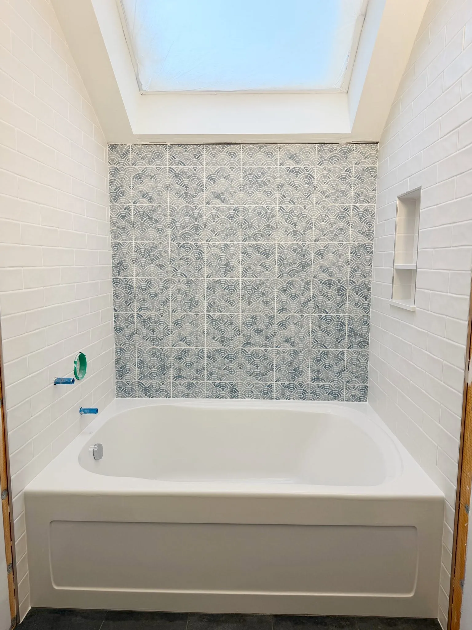 Bathtub surround with white subway tile and a gray wave-pattern accent wall