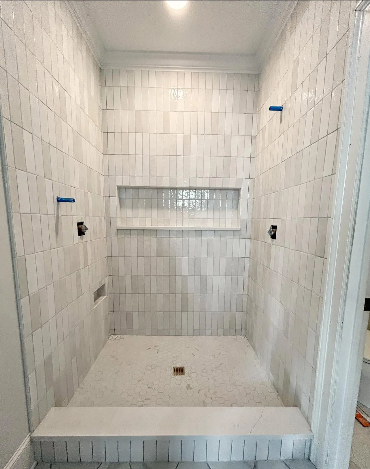 White tile walk-in shower installation with a long recessed niche and hex mosaic floor
