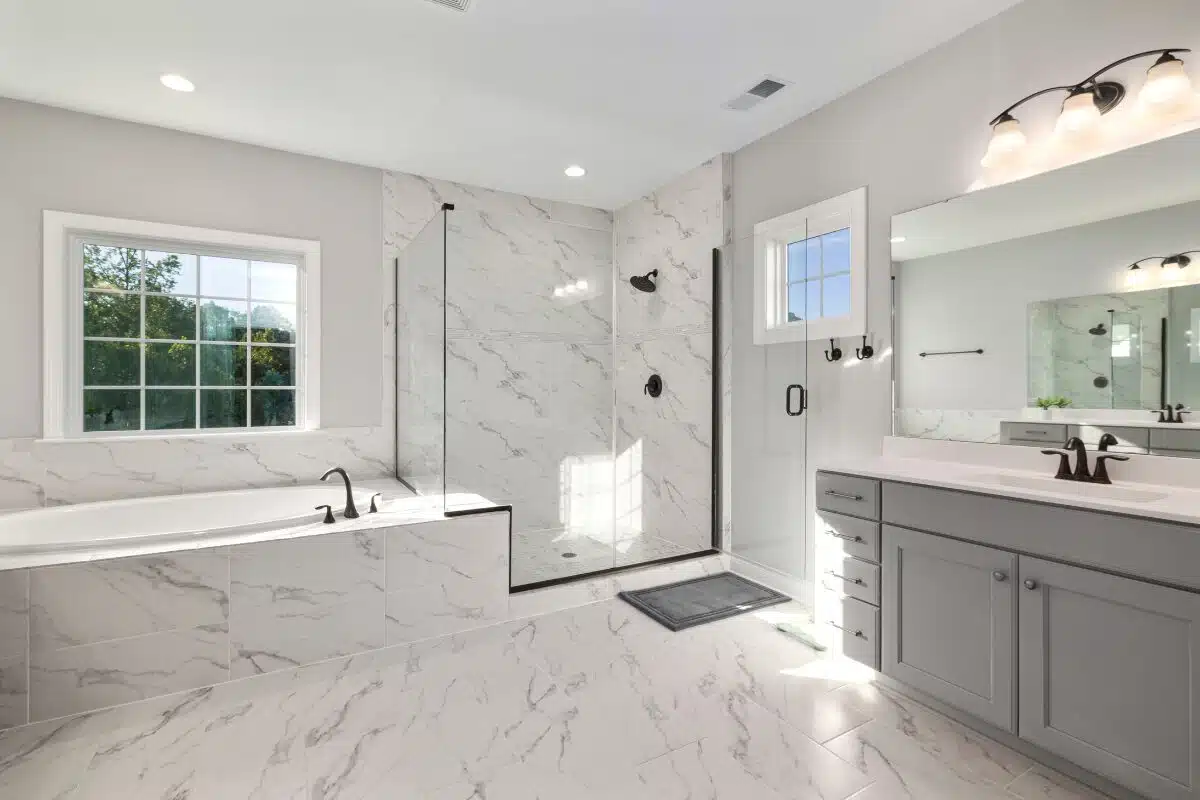 Bathroom remodel featuring a large remodeled bathroom with marble tile, large glass walk-in shower, and gray vanity.