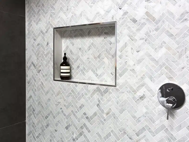 Tile installation in Cincinnati featuring a close-up of a shower wall with herringbone marble tile and a shower shelf.